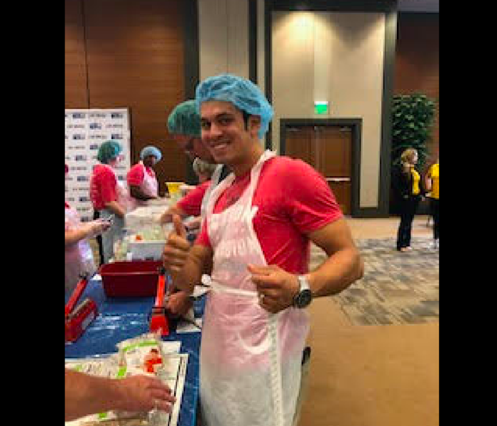 Male team member wearing a blue hair net and pink shirt while volunteering. 